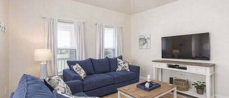 A living room with a blue sofa, a coffee table, a TV on a white cabinet, and a ceiling fan.