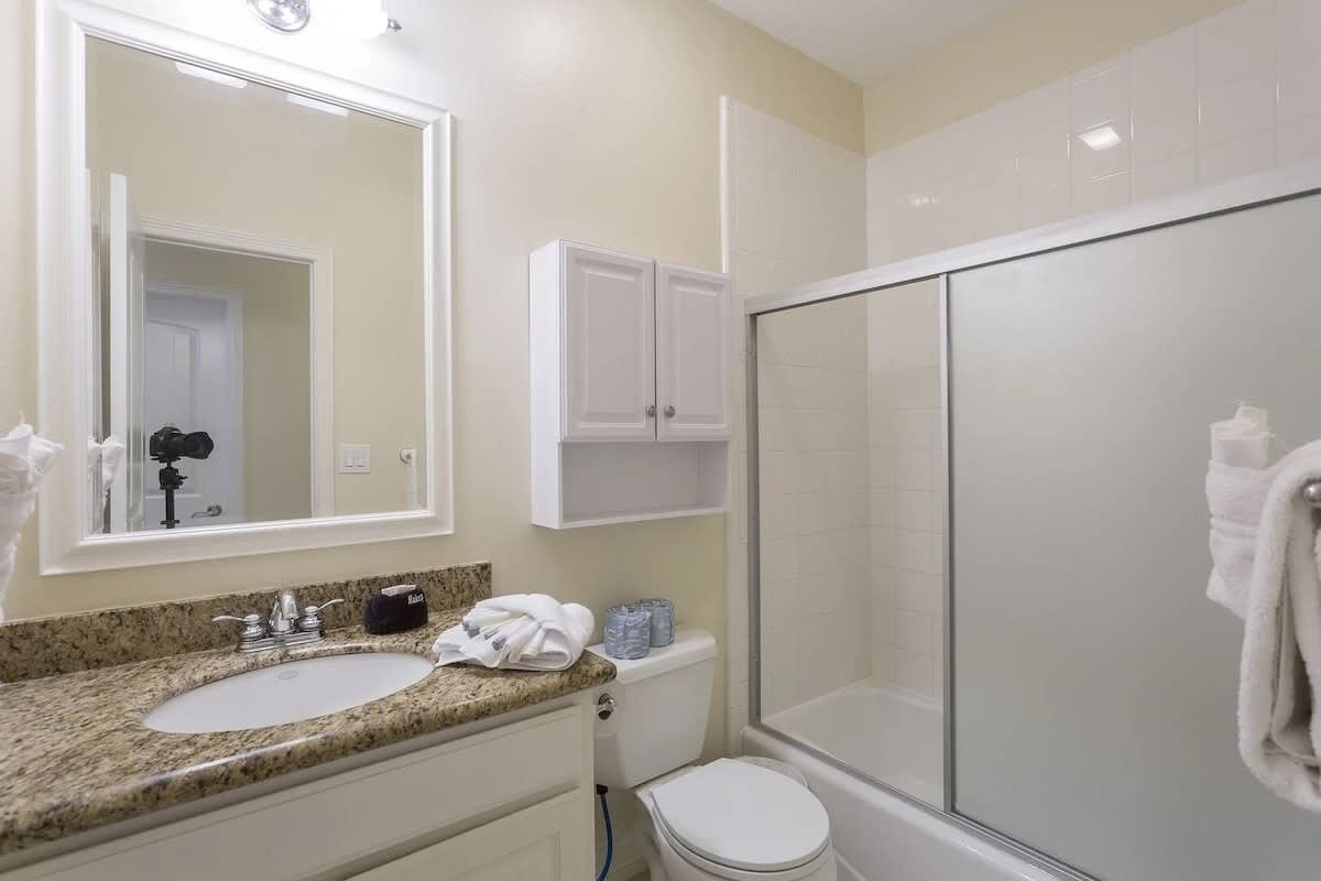 Un baño con lavamanos de encimera de granito, un espejo, inodoro y ducha con mampara de vidrio.