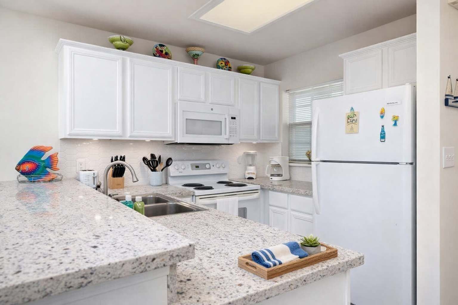 A modern kitchen with white cabinets, a granite countertop, a stove, a refrigerator, and decorative bowls on the shelf.
