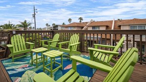 A deck with green Adirondack chairs, a colorful rug, and a view of residential buildings.