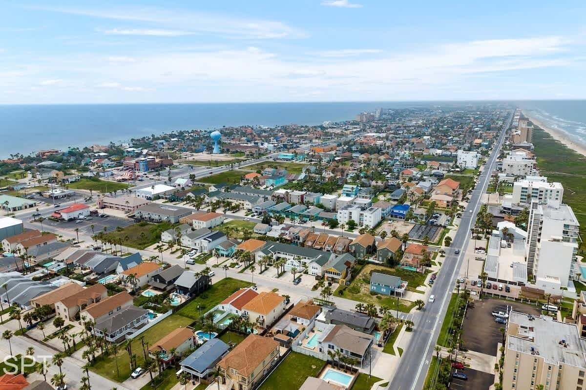 An aerial view of a coastal residential area with houses, roads, and a beach.