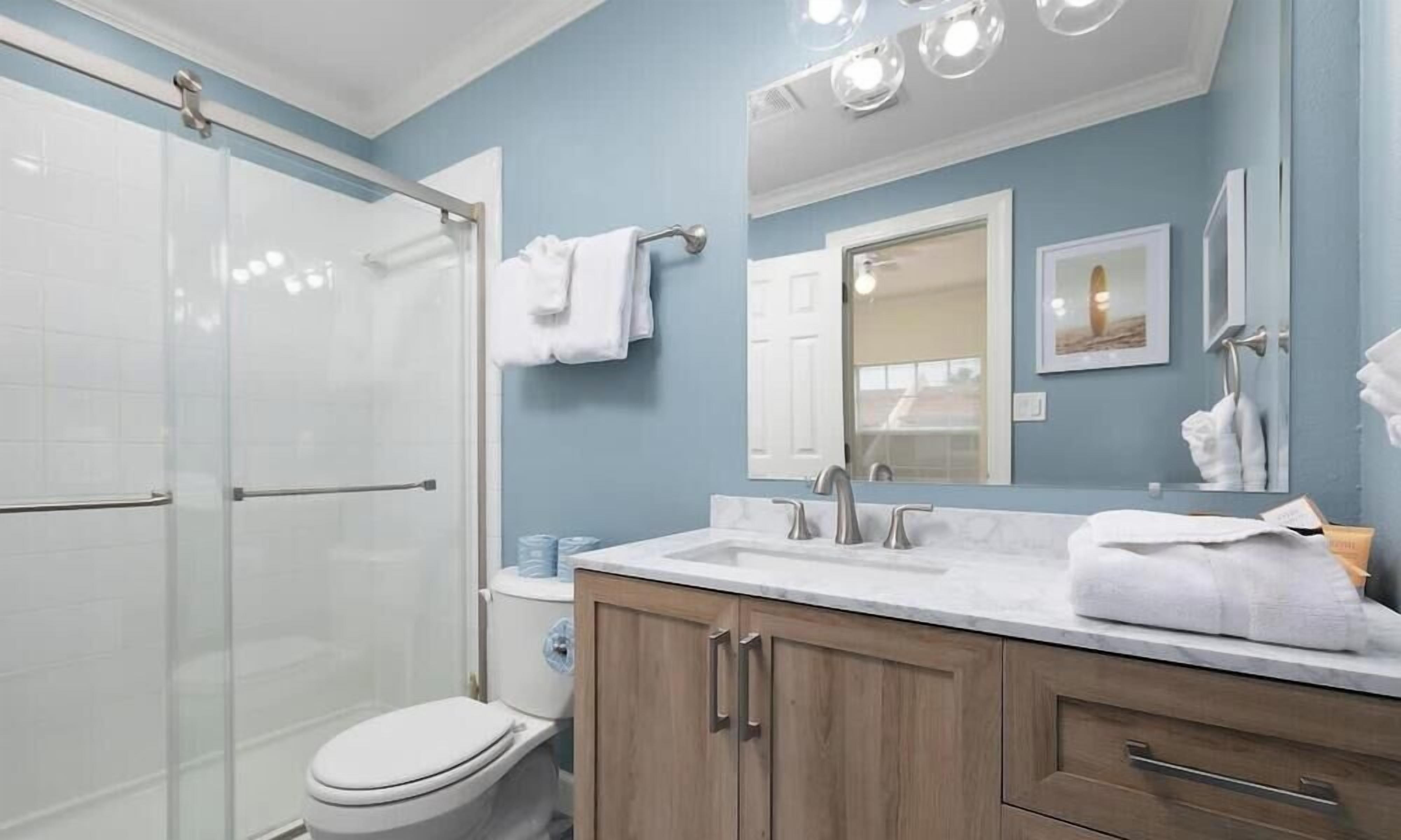 Une salle de bain avec une douche à parois de verre, des toilettes blanches, des meubles en bois, un lavabo en marbre et un grand miroir.