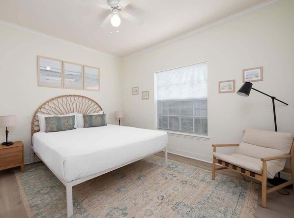 Un dormitorio con cama, una silla, una ventana con persianas e imágenes enmarcadas en la pared.