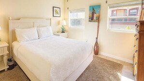 A neatly arranged bedroom with a large bed, bedside tables, a lamp, a vase, and a window with a view. - Pompano Beachview Home 4 Bedroom Home by RedAwning (South Padre Island)