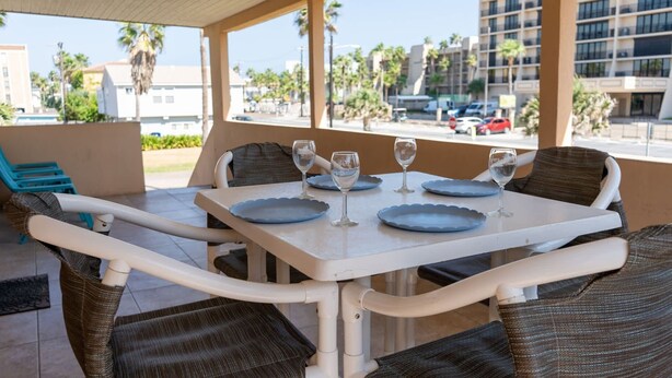 A covered outdoor dining area with a table set for four, featuring blue plates and wine glasses. - Pompano Beachview Home 4 Bedroom Home by RedAwning (South Padre Island)