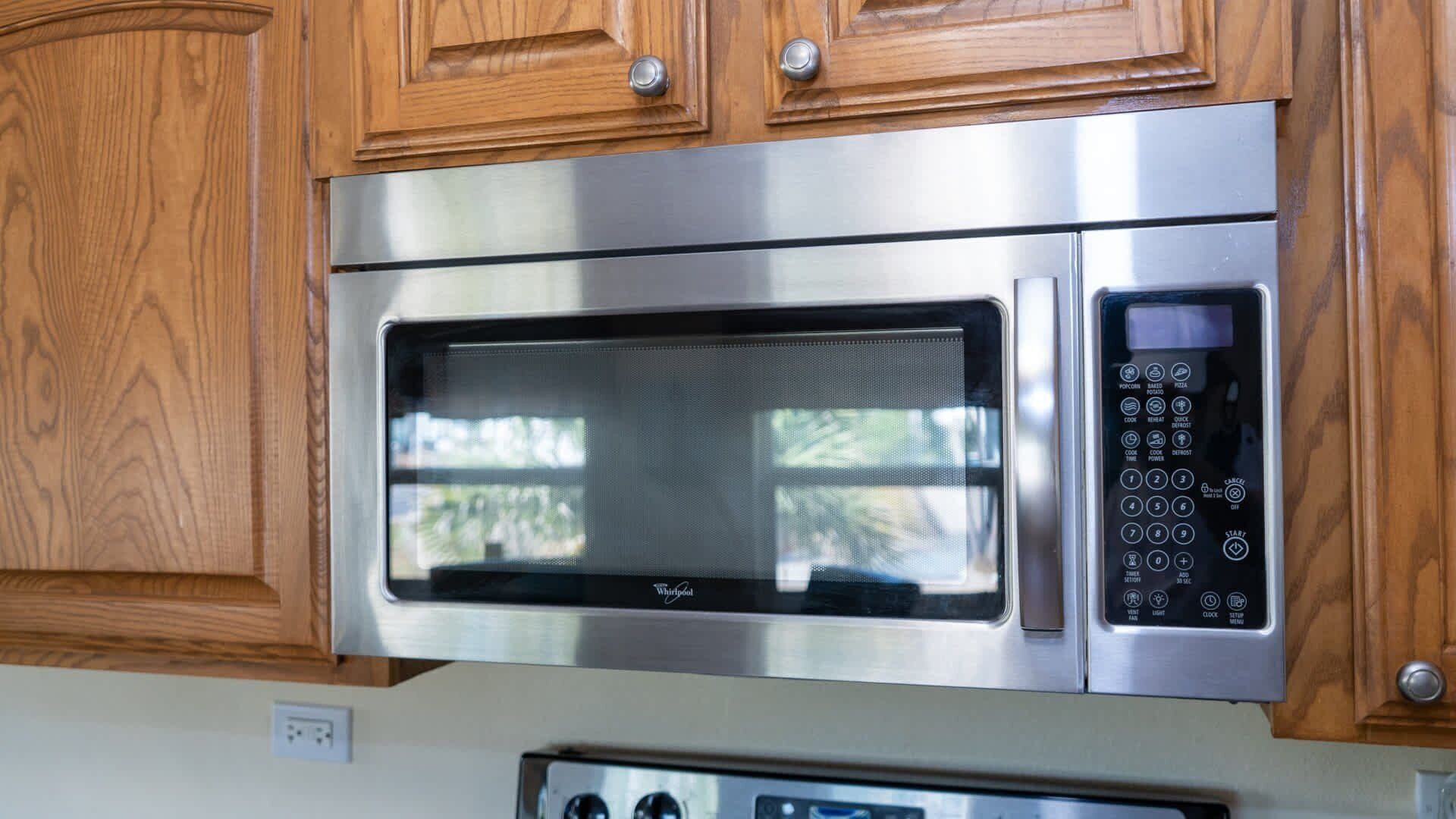 A stainless steel microwave oven with a digital control panel, housed in a wooden cabinet.