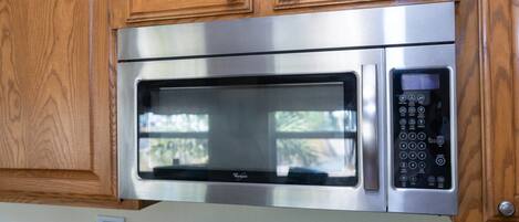 A stainless steel microwave oven with a digital control panel, housed in a wooden cabinet.