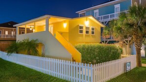 A two-story house with a white picket fence, a staircase leading to the upper floor, and a well-lit front porch. - Pompano Beachview Home 4 Bedroom Home by RedAwning (South Padre Island)