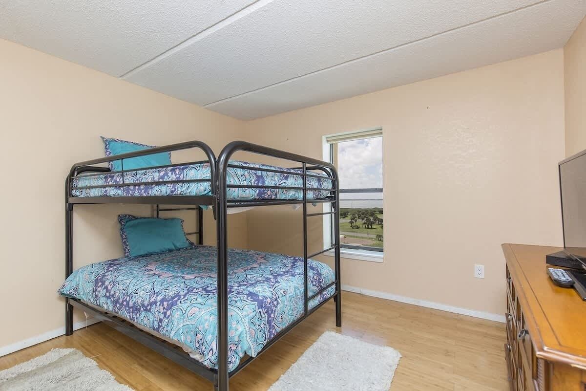 Quarto com beliche, colcha estampada, janela pequena e escrivaninha de madeira com um computador.