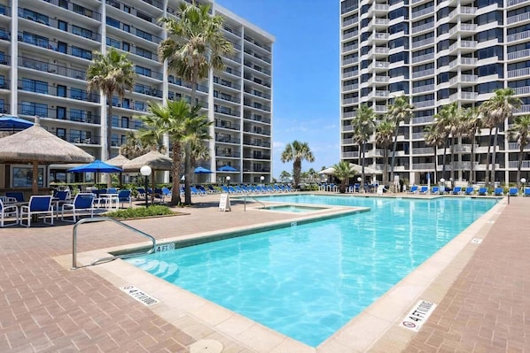 A hotel pool area with lounge chairs, palm trees, and a clear blue pool.