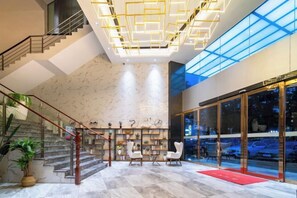 A hotel lobby with a marble floor, a staircase, a reception desk, and a glass door entrance.