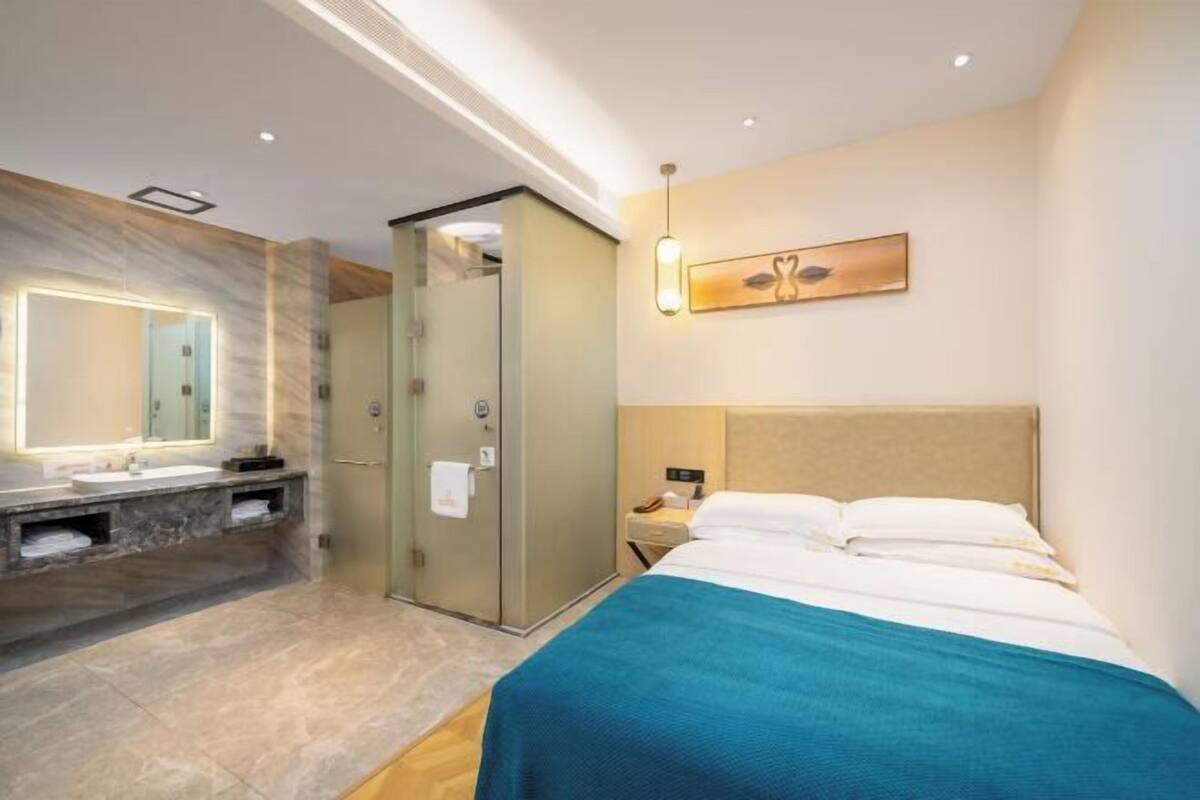 Une chambre d’hôtel moderne dotée d’un grand lit, d’une salle de bain séparée avec une douche en verre et d’une œuvre d’art accrochée au mur.