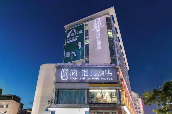 Een hotel met een opvallend bord met daarop Jian Shi Guang Hotel, met een modern ontwerp en een groot digitaal reclamebord aan de zijkant.