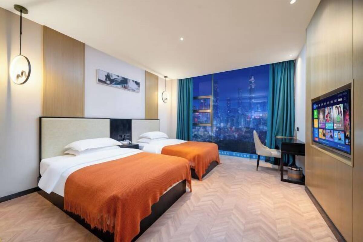 Une chambre d’hôtel avec deux lits, un bureau, une chaise et une grande fenêtre donnant sur le paysage urbain.