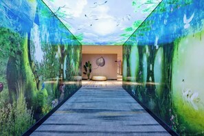 A corridor with a carpet, a round seating area, and walls with nature-themed murals.