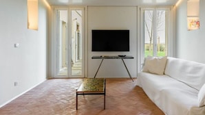 Ein modernes Wohnzimmer mit einem an der Wand montierten Flachbildfernseher, einem weißen Sofa, einem Couchtisch und großen Glasüren, die zu einem Außenbereich führen.