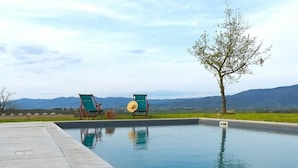Ein rechteckiger Pool mit zwei grünen Liegestühlen, auf einem davon liegt ein Hut. Um den Pool erstreckt sich eine Betonplattform mit Blick auf die Berge im Hintergrund.