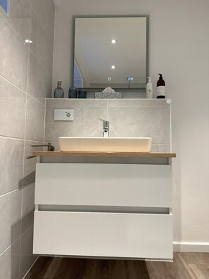 Une salle de bain moderne avec un grand miroir, un lavabo sur colonne et une étagère en bois.