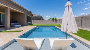 Una piscina con dos sillas de descanso blancas y una sombrilla blanca.