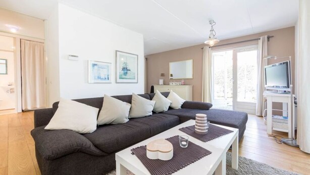 A modern living room with a dark grey sofa, white coffee table, and a television on a stand. - Holiday Home Dune Nest (Noordwijk)