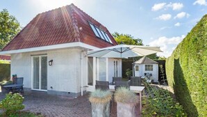 A house with a red roof, a white exterior, and a covered patio area with outdoor furniture. - Holiday Home Dune Nest (Noordwijk)