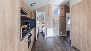 A compact kitchen with wooden cabinets, a stove, and a countertop with fruits. There is a ladder leaning against a wall and a door leading to another room. - Chalet With Covered Terrace in the Leukermeer (Well)