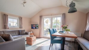A cozy living room with a sofa, a dining table, and a TV. - Chalet With Covered Terrace in the Leukermeer (Well)
