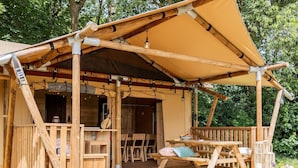 Una cabaña de madera con porche cubierto, mobiliario exterior y una pequeña mesa.
