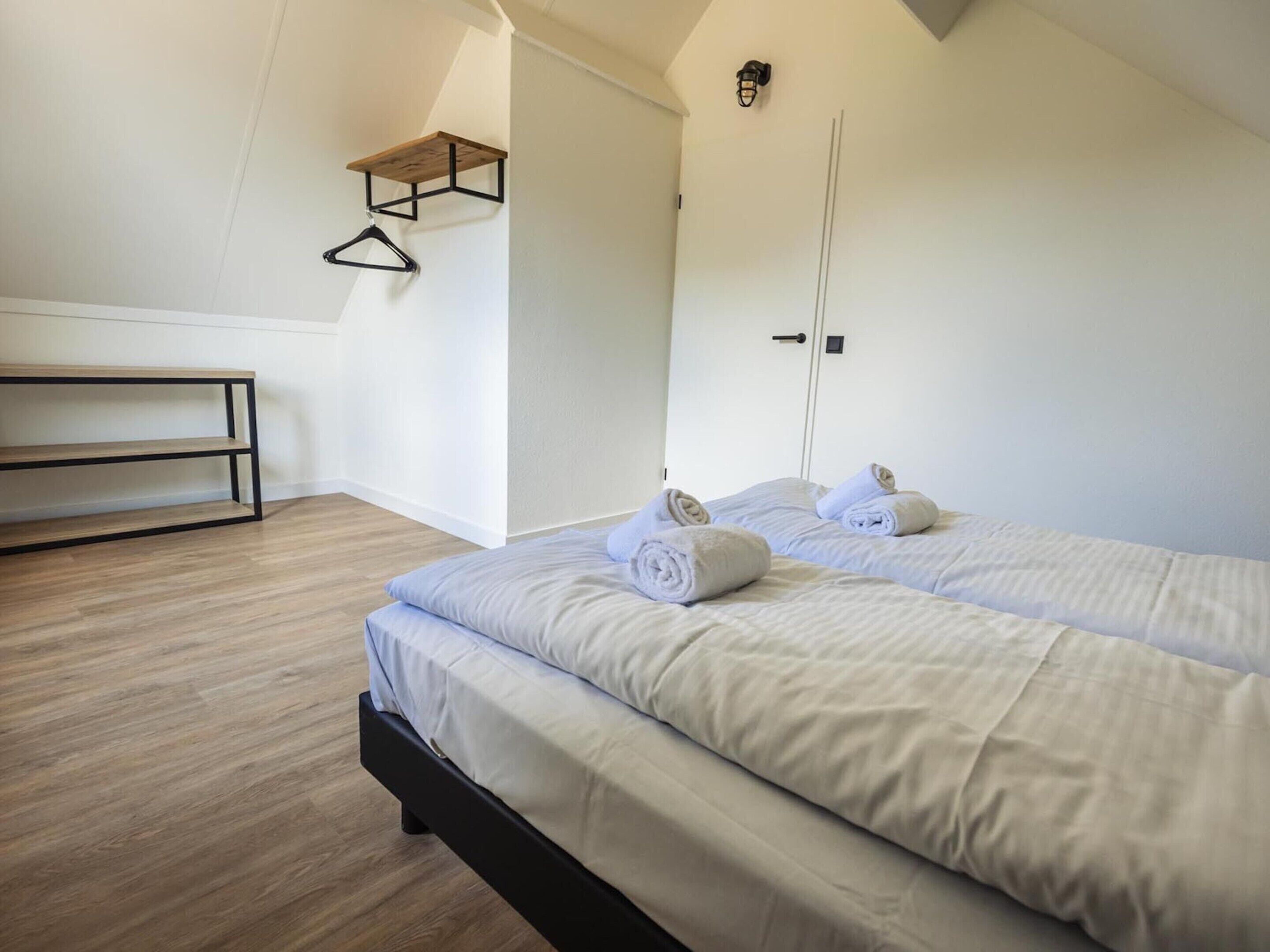 A bedroom with two beds, a wooden bench, and a wall-mounted towel rack.