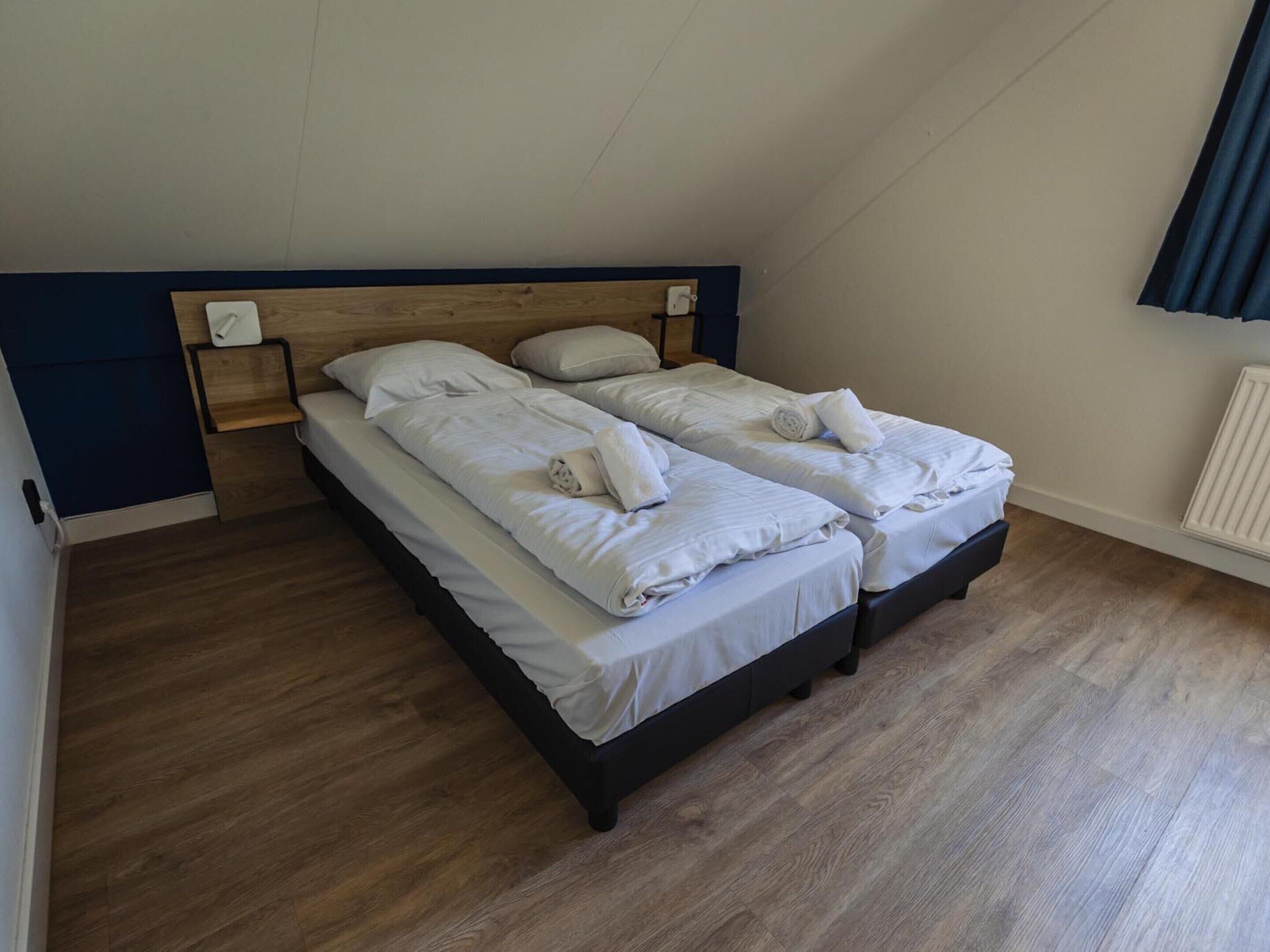 Una habitación con dos camas, suelo de madera y cabecera azul oscuro.