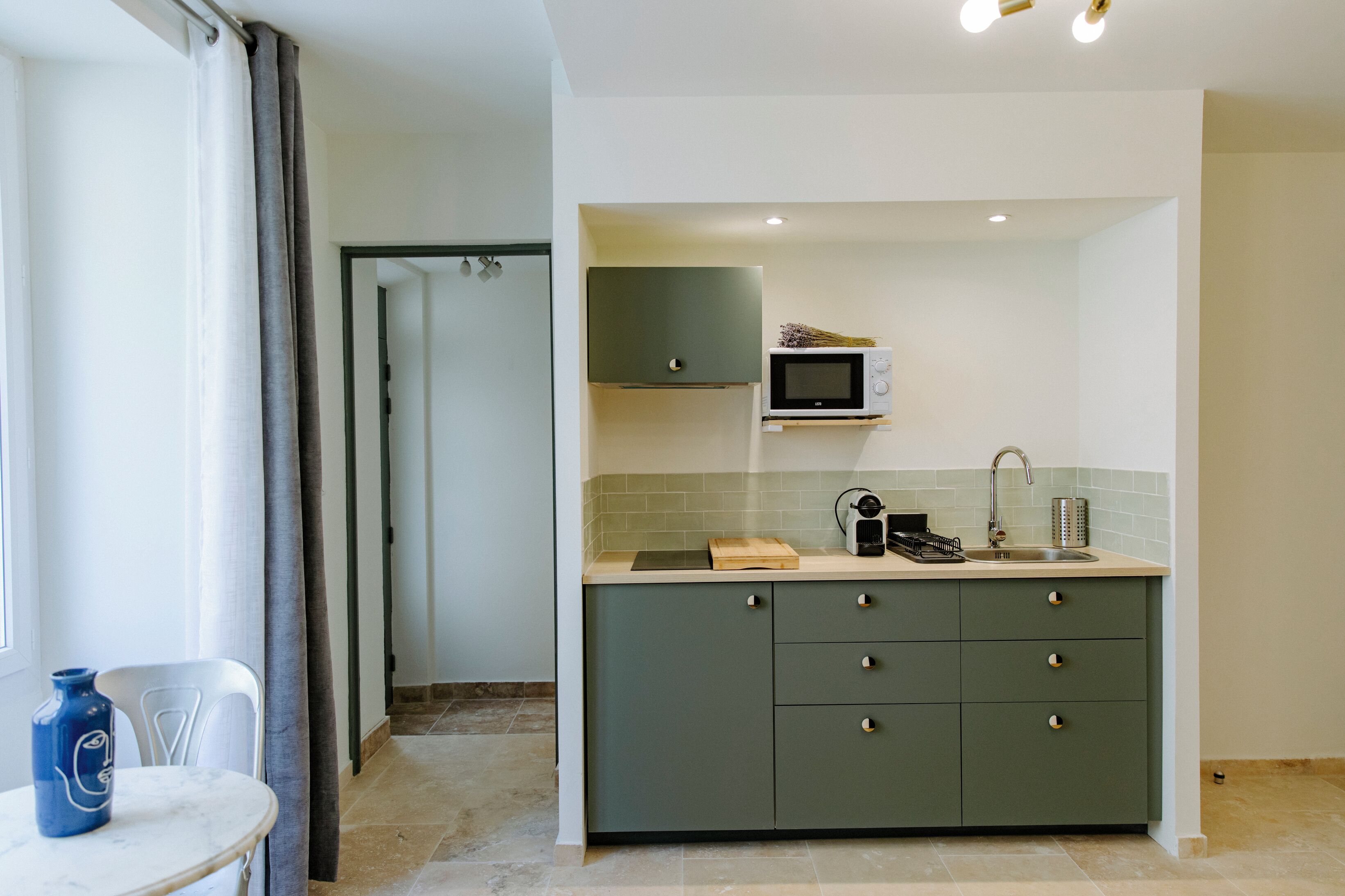 A compact kitchen with a microwave, sink, and green cabinets.