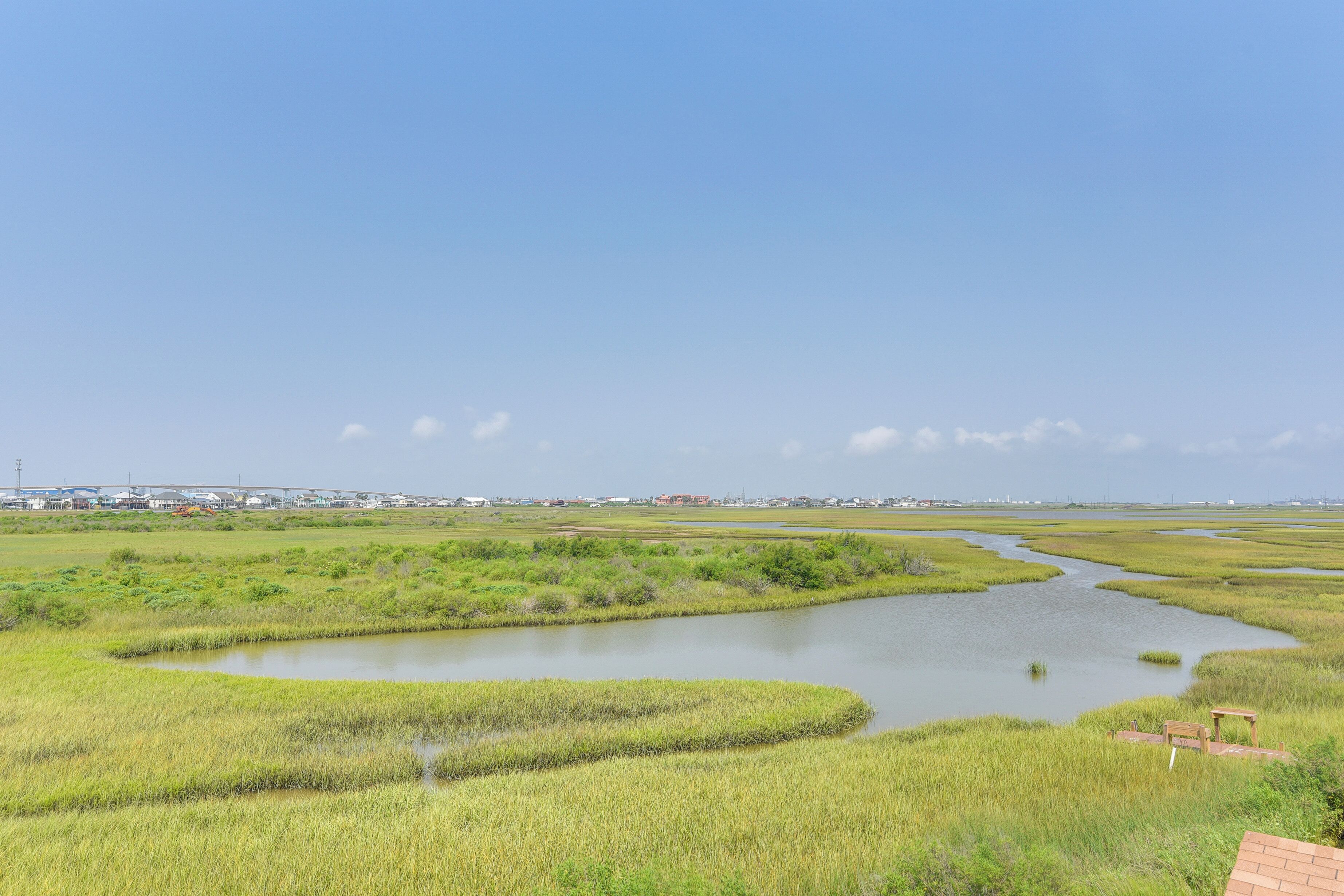 Paesaggio paludoso con un fiume, edifici in lontananza e cielo sereno.