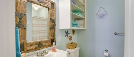 A bathroom with a wooden vanity, a toilet, and a shelf with towels.