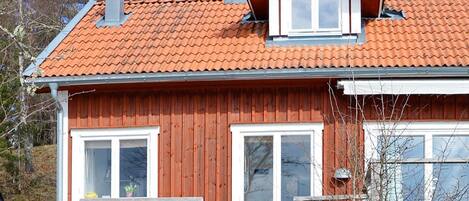 A two-story house with a red-tiled roof, white-framed windows, and a visible chimney.