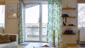 A room with a sofa, a table with a book, a window with a curtain, and a view of the outdoors. - 5 Star Holiday Home in Hjaltevad (Hjältevad)