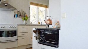 A kitchen with a white tiled backsplash, a stainless steel range hood, a white oven, a black stove, and a window with a view of trees. - 5 Star Holiday Home in Hjaltevad (Hjältevad)