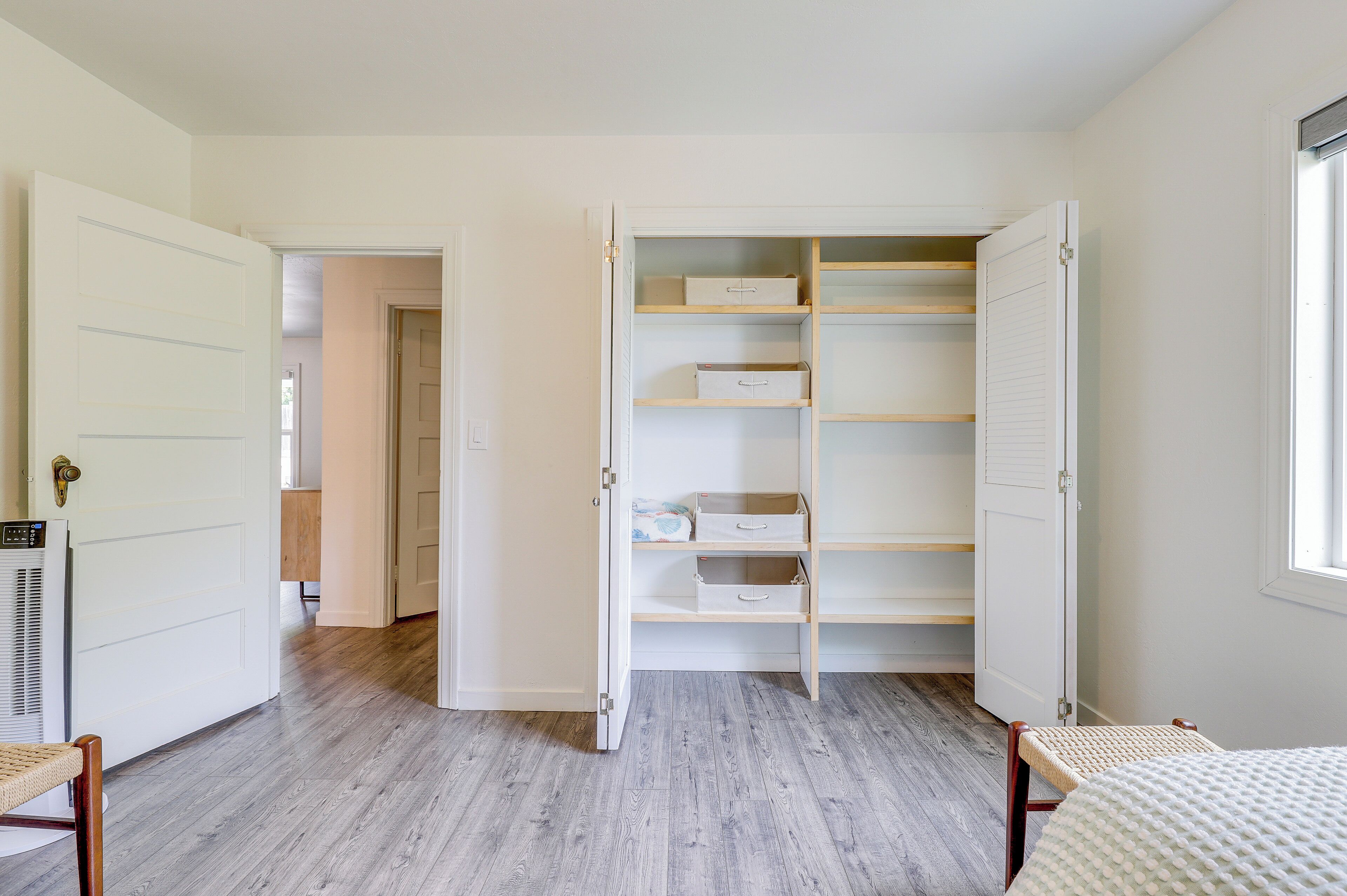 A room with a wooden floor, a white wardrobe with open doors, and a window on the right.