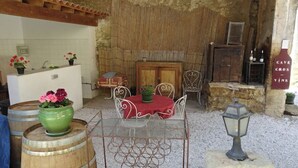 Een rustieke buitenruimte met een tafel, stoelen, een houten kast en een bord met een wijnfles.