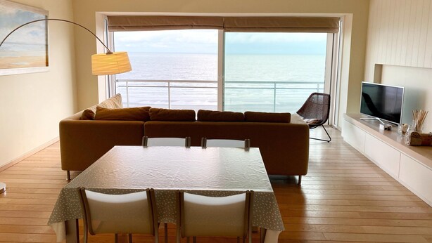 Un salon comprenant un canapé, une table à manger, des chaises, un téléviseur et une vue sur l’océan.