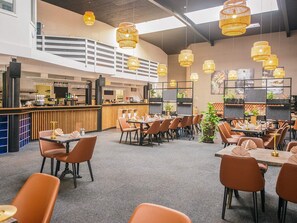Ein modernes Restaurant mit hohen Decken, hängenden Korblampen und einem Barbereich.