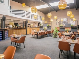 Un restaurante moderno con techos altos, lámparas de mimbre colgantes y una zona de bar.