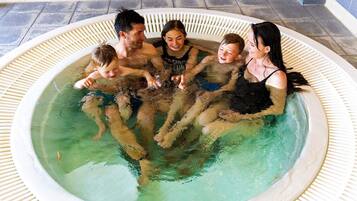 A group of people in a hot tub with a tiled floor and a white wall in the background.