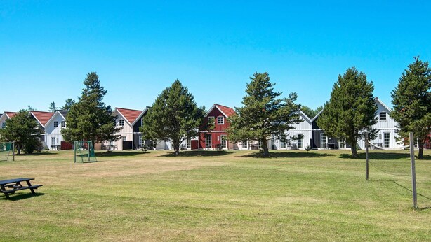 A grassy area with a picnic table, trees, and a row of buildings with red roofs. - 8 Person Holiday Park Home in Blavand (Blavand)
