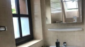 Un baño con ventana, lavamanos, espejo y radiador.