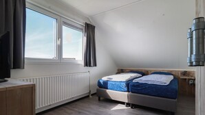 Makuuhuone, jossa on sänky, ikkuna, patteri, puinen työpöytä ja televisio.