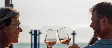 Two people toasting with wine glasses at a seaside table with an umbrella.