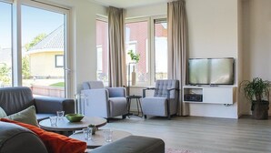 Un salon moderne avec un canapé gris, deux fauteuils, une table basse et un téléviseur à écran plat fixé au mur.