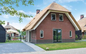 Une maison en briques avec un toit de chaume, une porte en verre et un petit jardin.