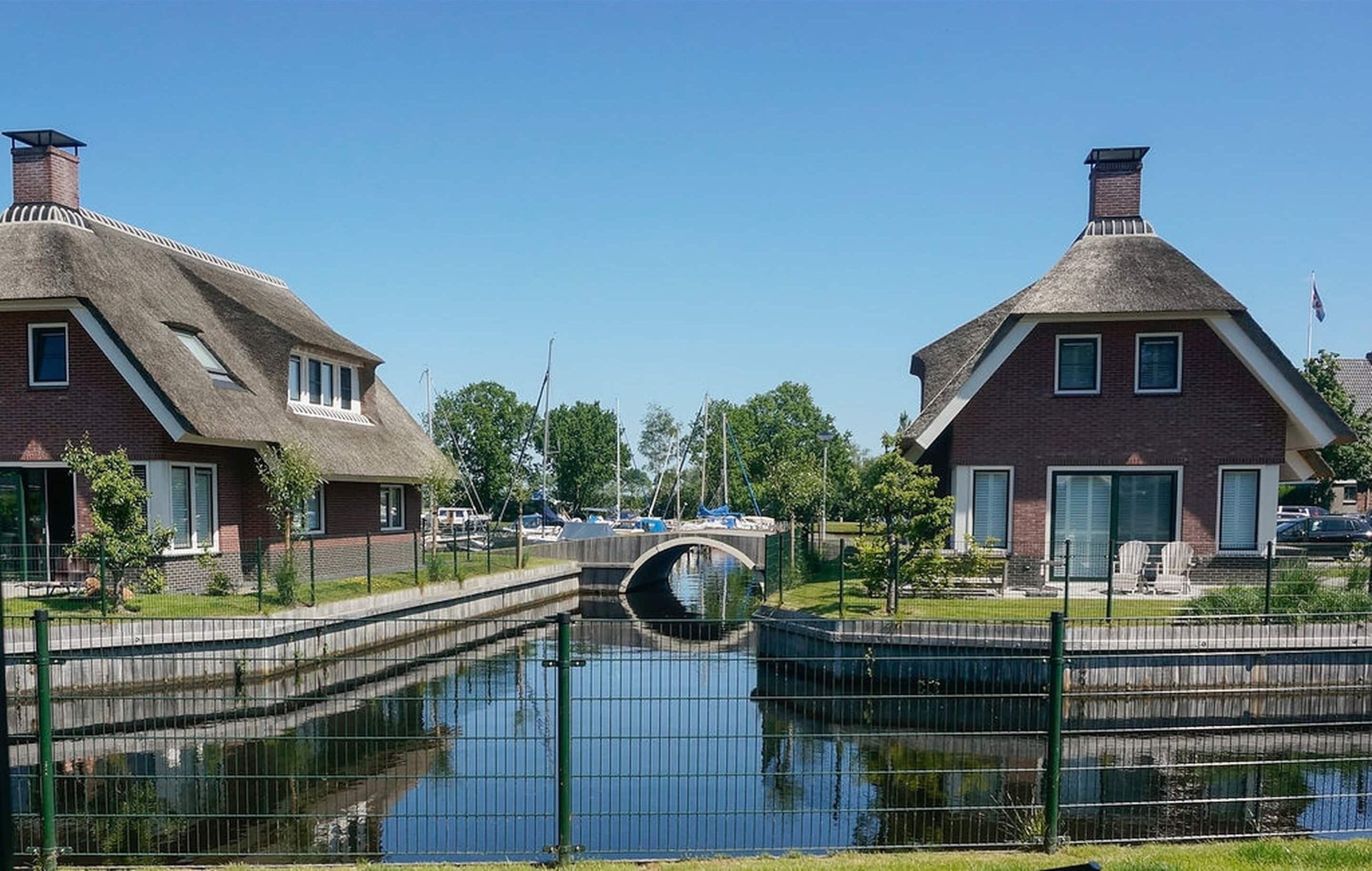A canal with houses on either side, a bridge, and a clear sky.
