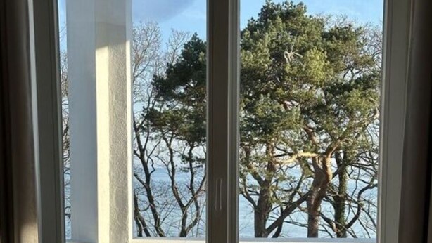 A room with a large sliding glass door leading to a balcony with a view of trees and a body of water. - Luxury & Design With sea View (Kuehlungsborn)